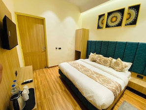 A hotel room with a bed, a TV, a wooden wardrobe, and a small table with a remote control and a bottle. - Hotel O Park Plaza (Amritsar)