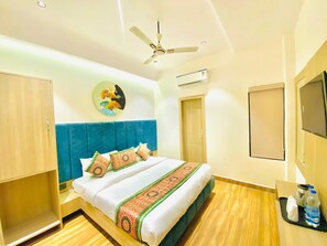 A hotel room with a bed, a ceiling fan, an air conditioning unit, a wall-mounted TV, and a wooden floor. - Hotel O Park Plaza (Amritsar)