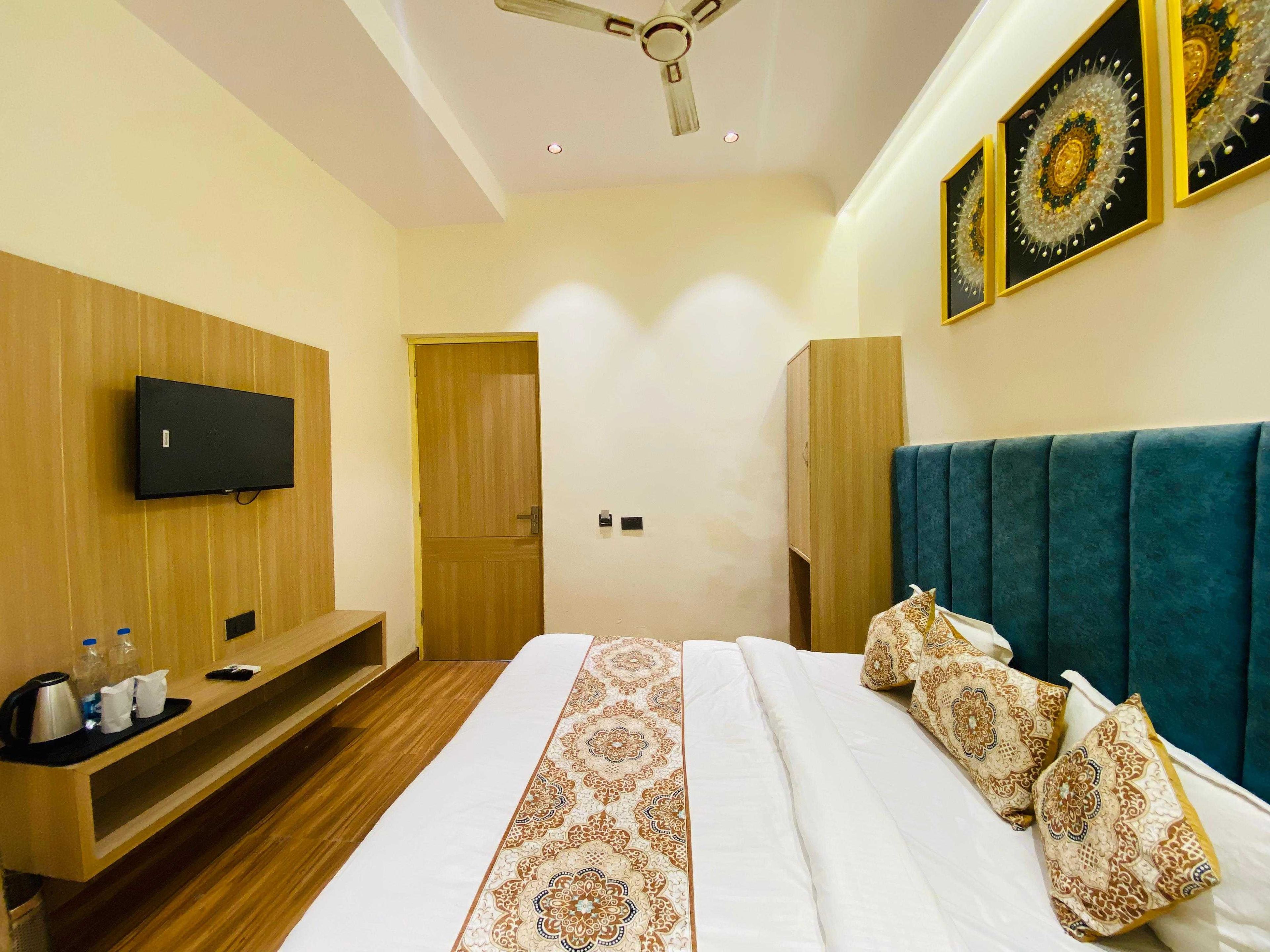 A hotel room with a bed, a television mounted on the wall, a wooden wardrobe, and a ceiling fan.