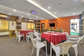 A dining area with round tables covered in red tablecloths, white plastic chairs, and a buffet setup with food containers. - Hotel O Rahul International Hyderabad (Hyderabad)
