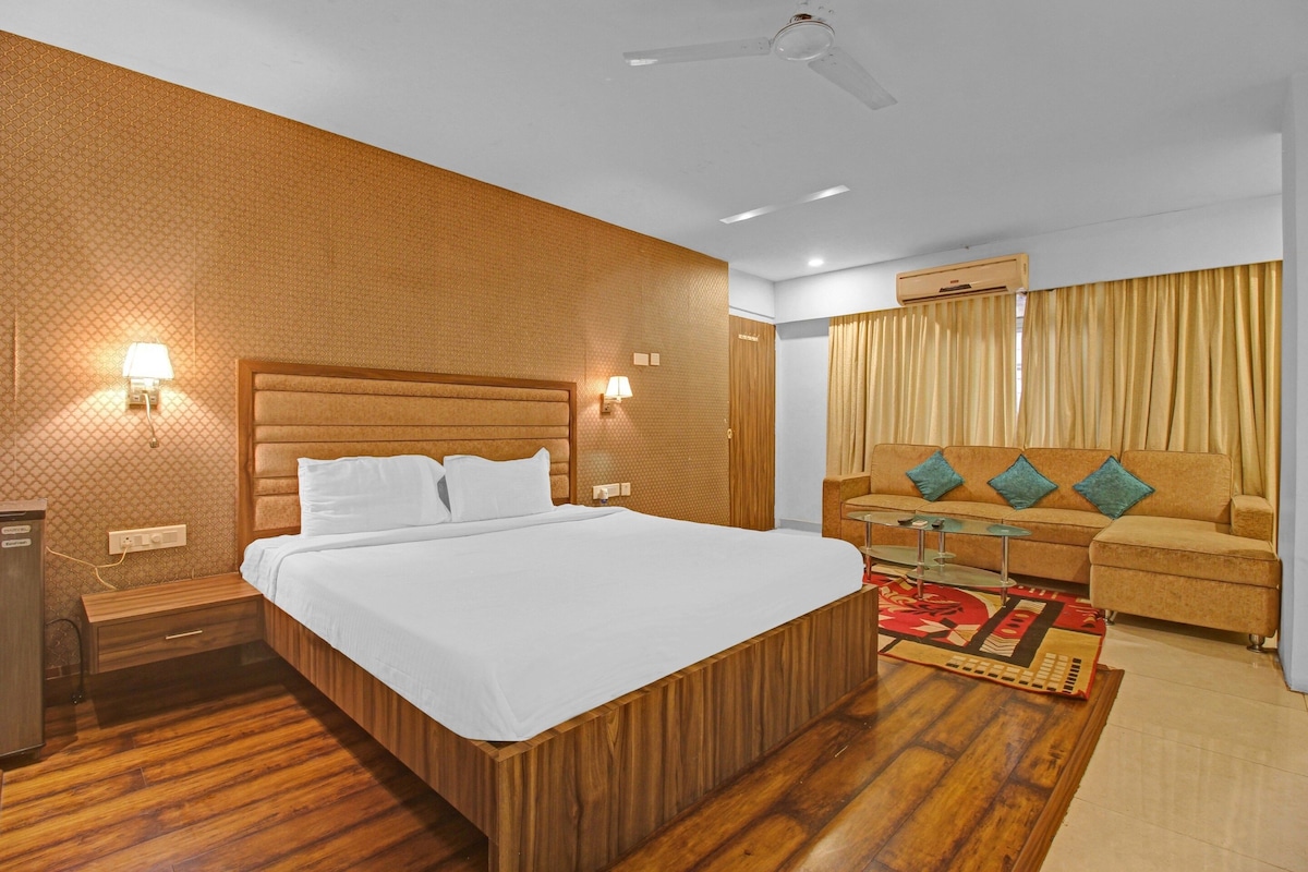 A hotel room with a wooden bed, a sofa, a glass coffee table, and a ceiling fan.
