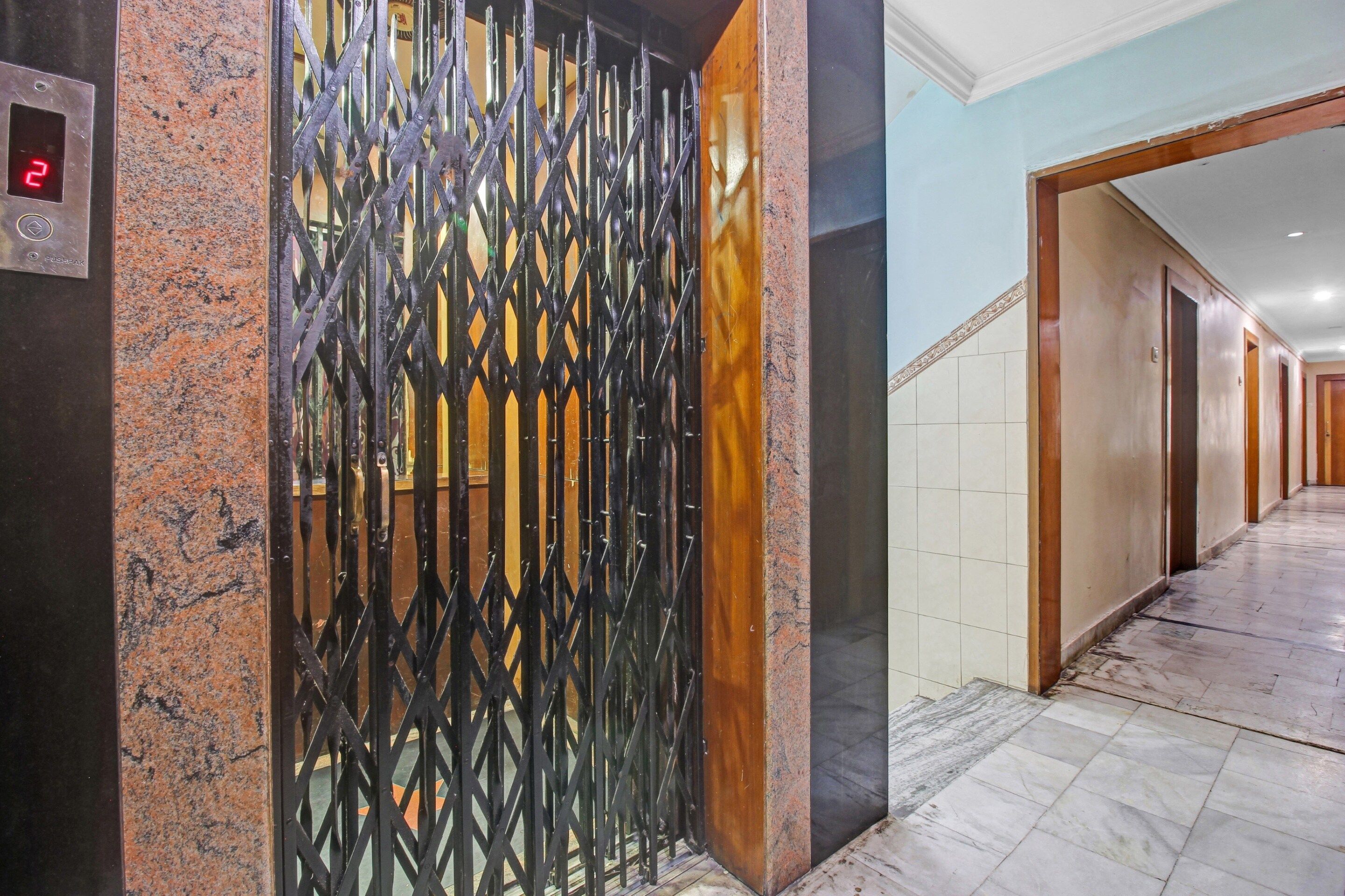 A hallway with a metal gate, marble flooring, and a series of doors.