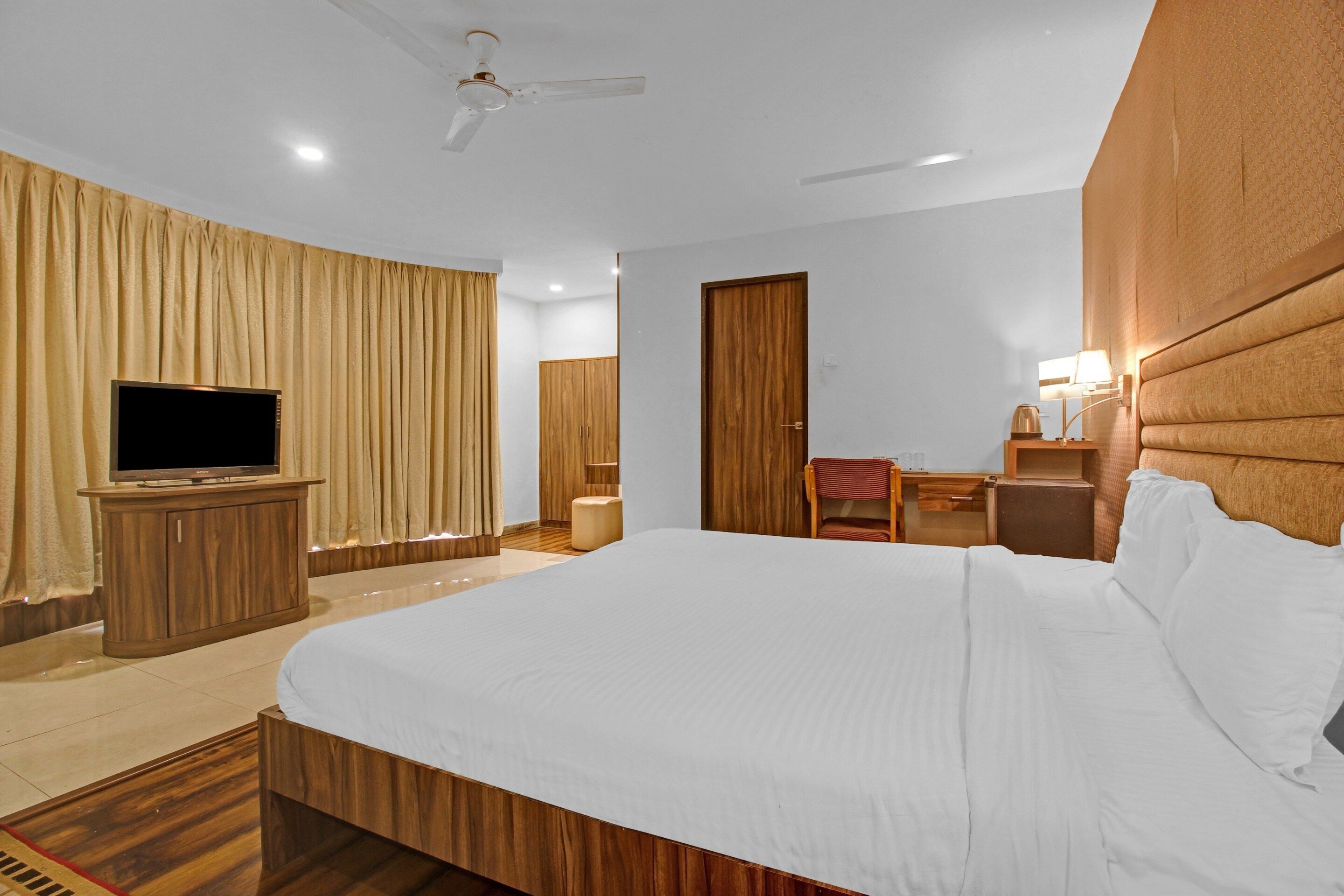 Habitación de hotel con una cama grande, televisor, escritorio con silla y armario.