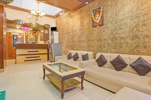 A reception area with a reception desk, a refrigerator, and a wall with a leaf pattern. There is a sofa with cushions and a glass-top coffee table. - Hotel O Rahul International Hyderabad (Hyderabad)