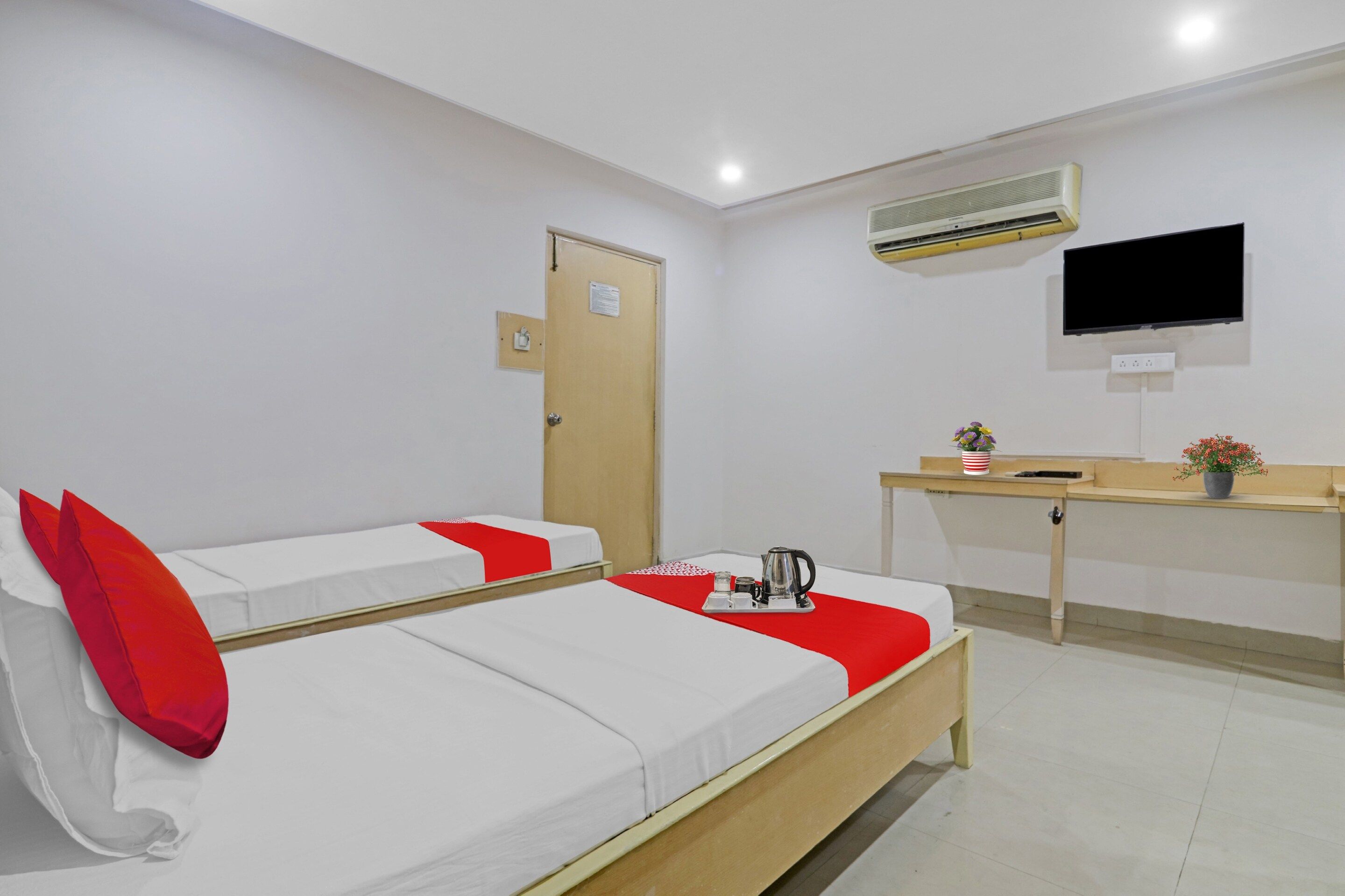 A hotel room with two beds, a desk, a television, and an air conditioning unit.