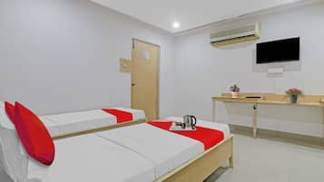 A hotel room with two beds, a desk, a television, and an air conditioning unit.