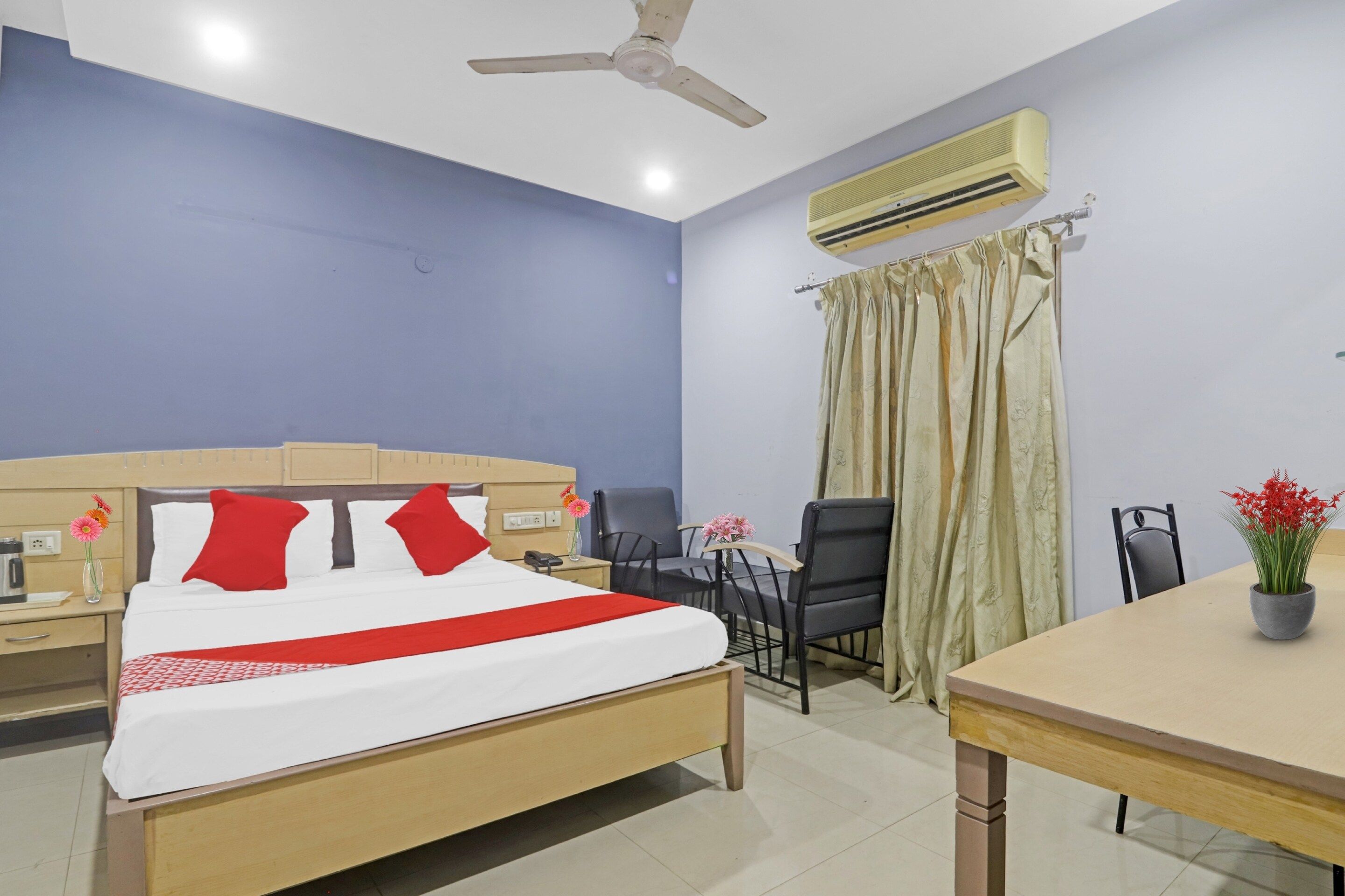 A hotel room with a bed, a desk, a chair, an air conditioner, and a ceiling fan.
