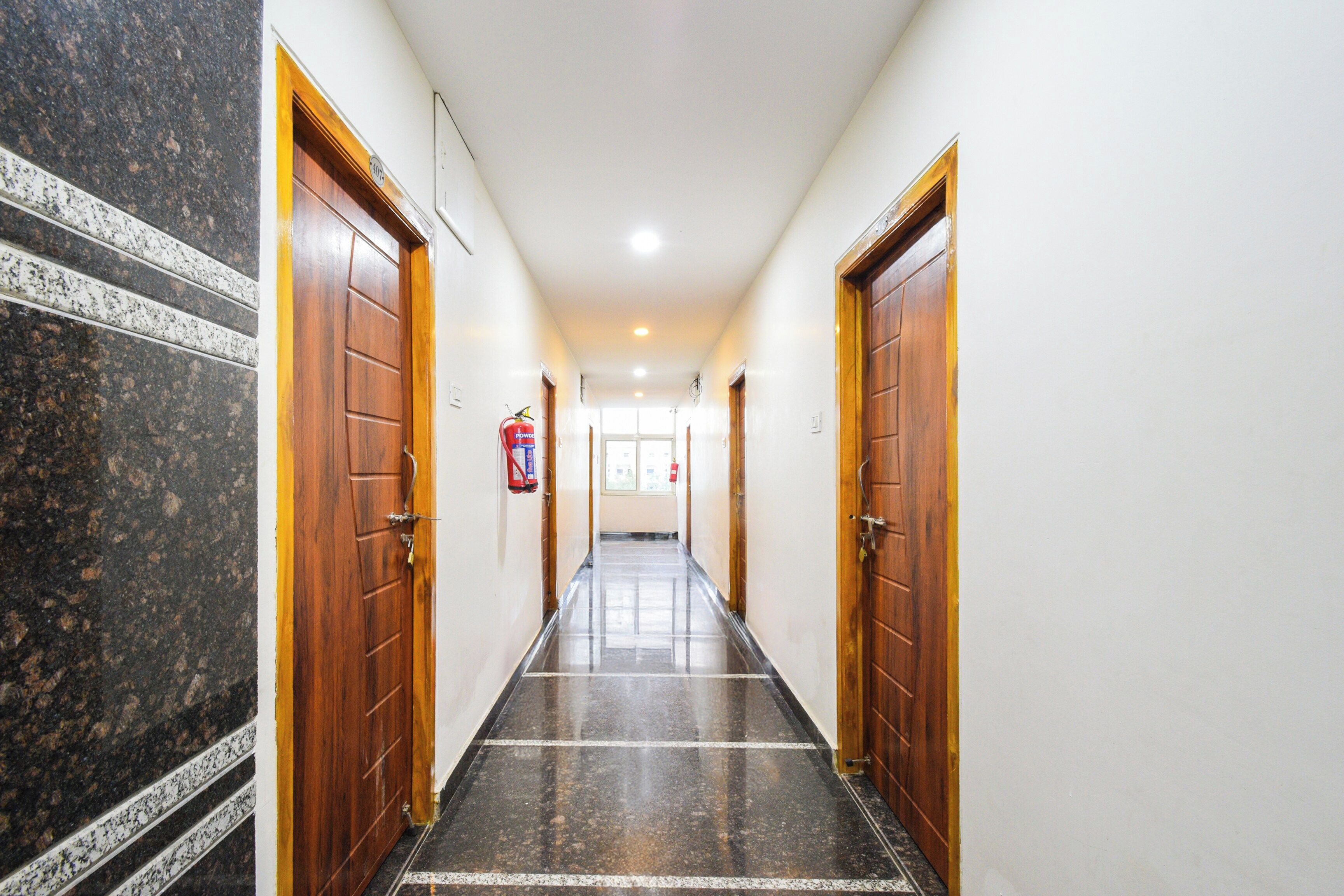 A corridor with wooden doors, a fire extinguisher, and a tiled floor.