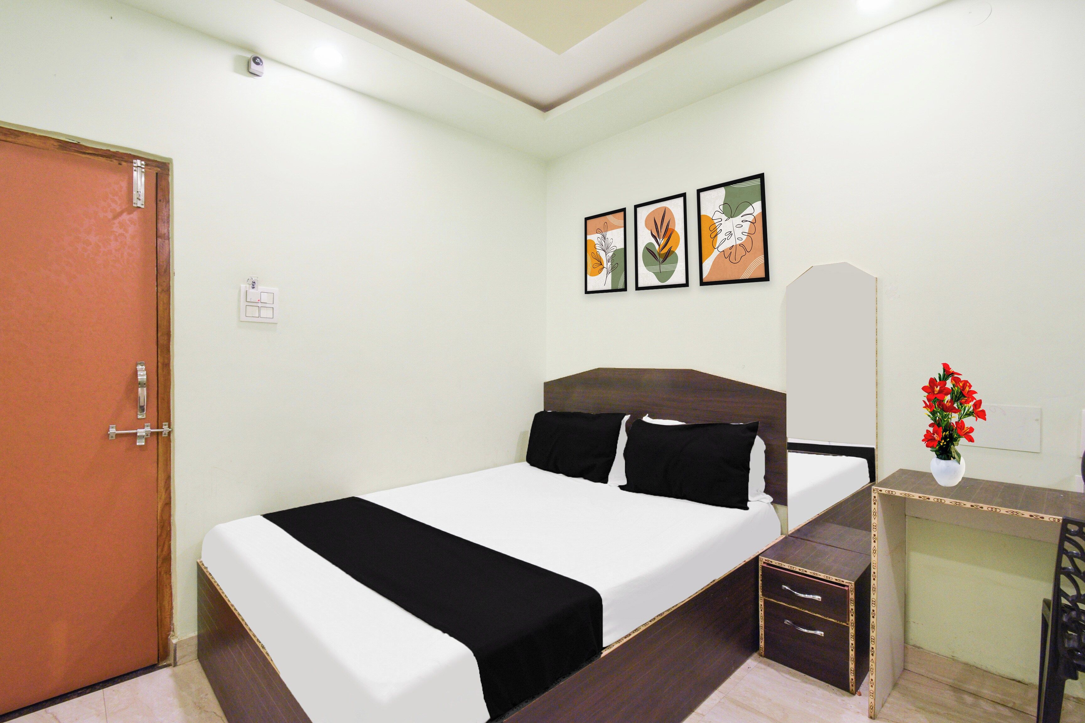 A hotel room with a bed, a desk, a chair, a door, and three framed artworks on the wall.