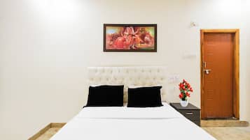 Una habitación de hotel con cama, un cuadro en la pared, una puerta y una mesita de noche con un jarrón de flores.