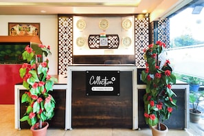A reception desk with a sign indicating it is company-serviced, surrounded by decorative plants and clocks displaying different time zones.