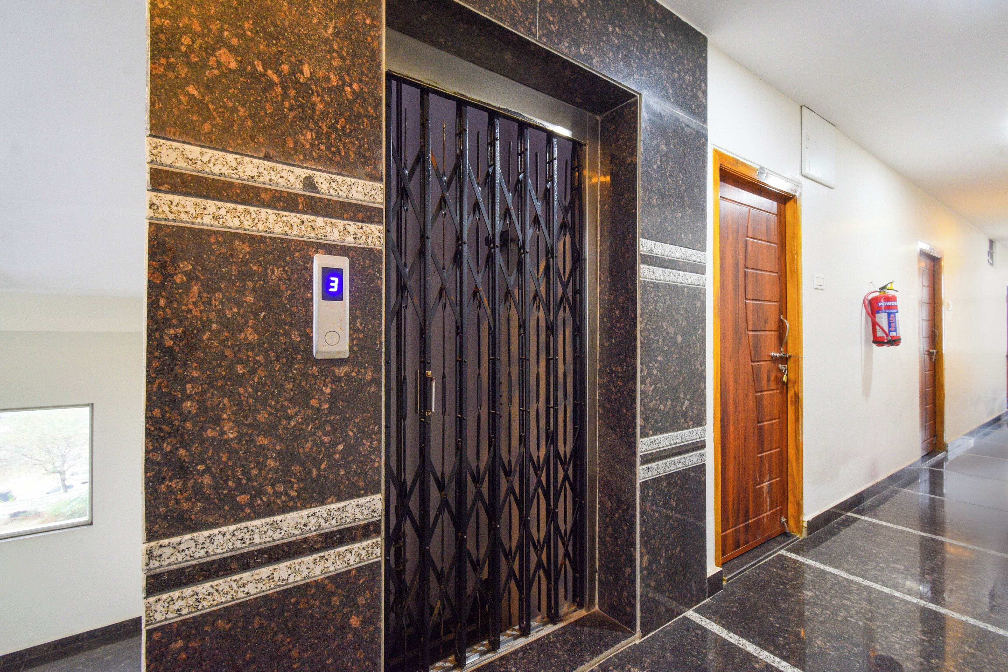 Un couloir avec une grille métallique, une porte en bois et un extincteur fixé au mur.