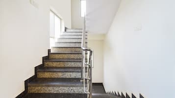 Una escalera con barandilla metálica, peldaños alfombrados y una pared blanca con un ventanal en la parte superior.