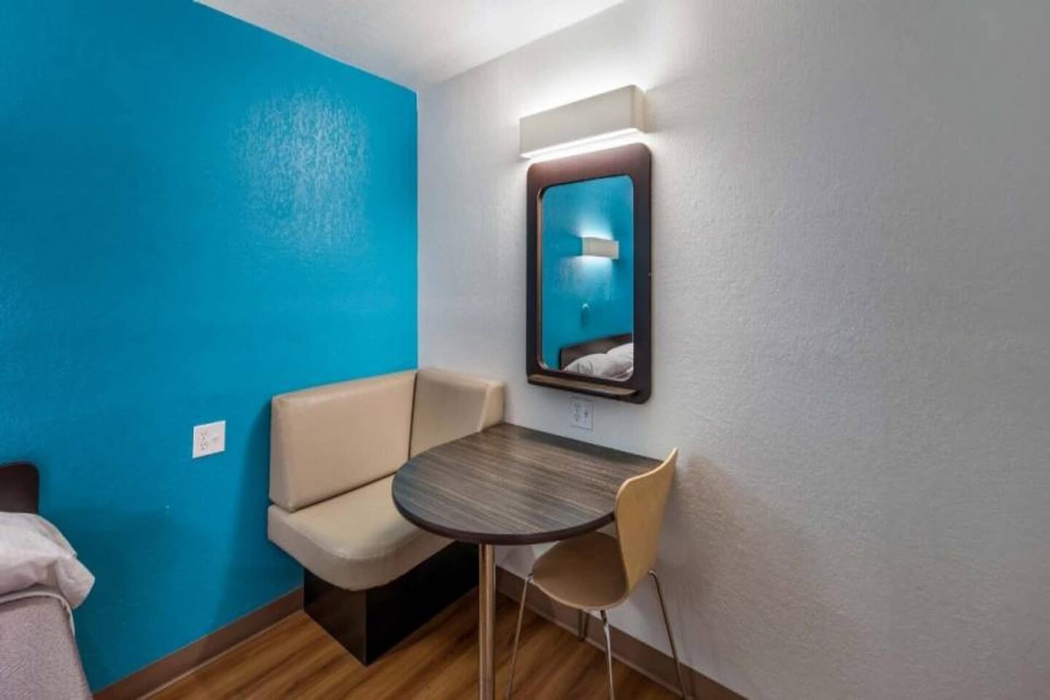 A small hotel room with a blue accent wall, a single bed, a round table with two chairs, and a mirror on the wall.