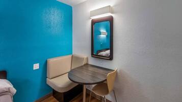 A small hotel room with a blue accent wall, a single bed, a round table with two chairs, and a mirror on the wall.