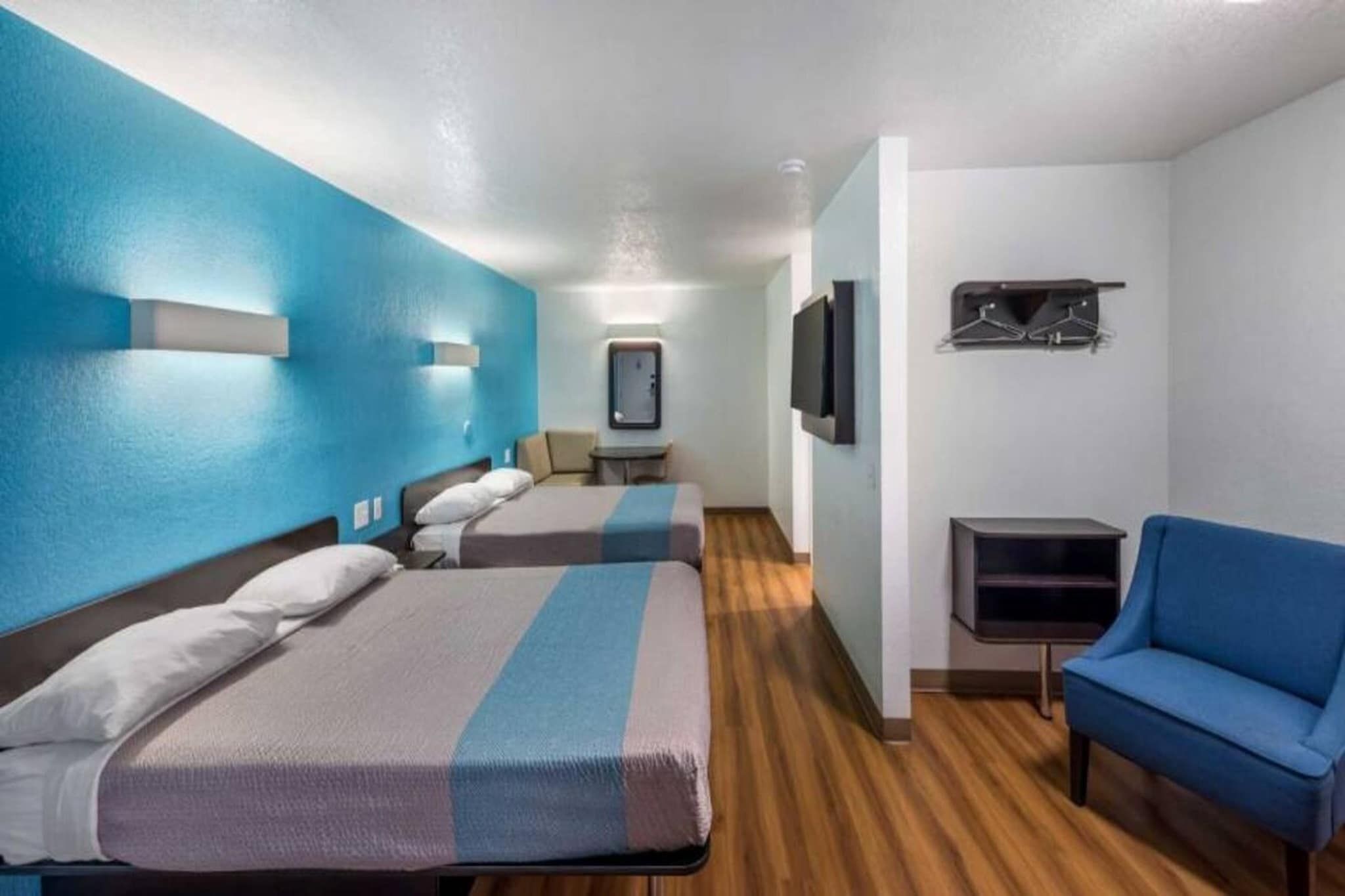 A hotel room with two beds, a desk, a chair, a TV, and a coat rack.