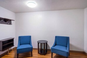 A room with two blue chairs, a small round table, and a dark wooden shelf against a white wall. - 2 Queen Beds | Smoking, Micfridge (Irving TX)