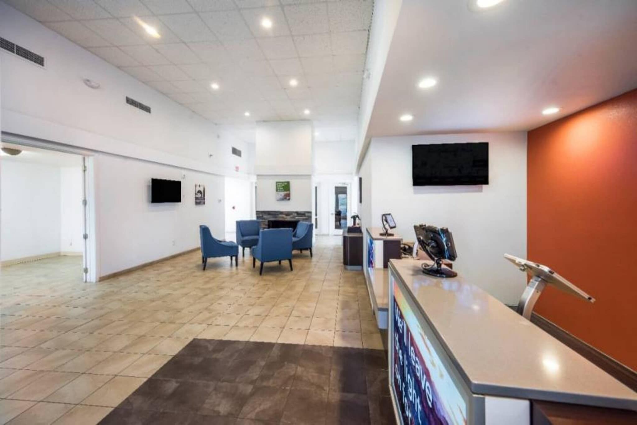 A spacious lobby with a reception desk, seating area, and a large screen.