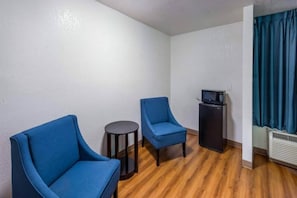 A small room with two blue chairs, a small table, a black cabinet with a television, and a window with blue curtains. - 1 King Bed | Smoking, Micfridge (Irving TX)