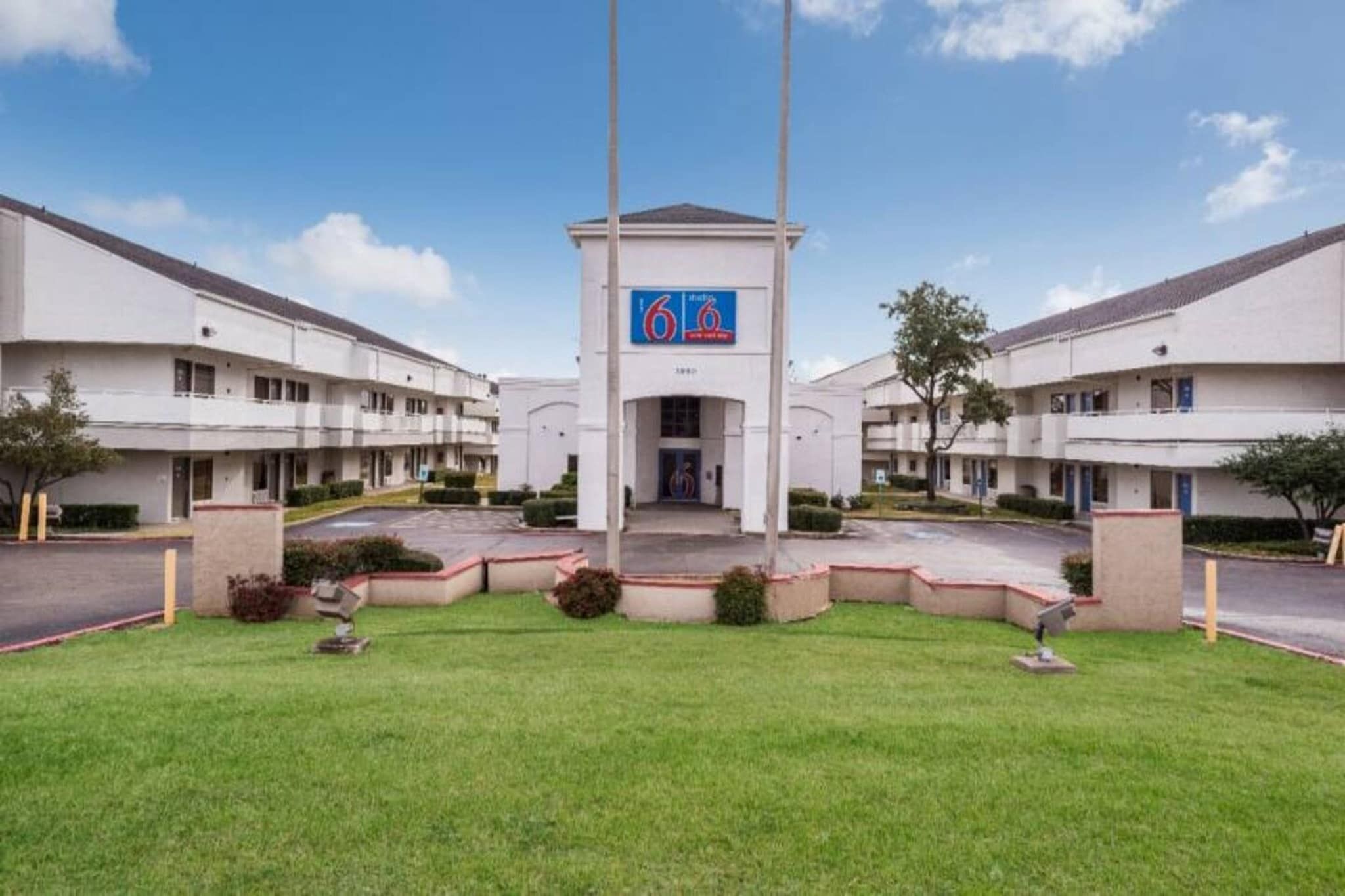 Un hotel con entrada central, varios pisos y zona de estacionamiento.
