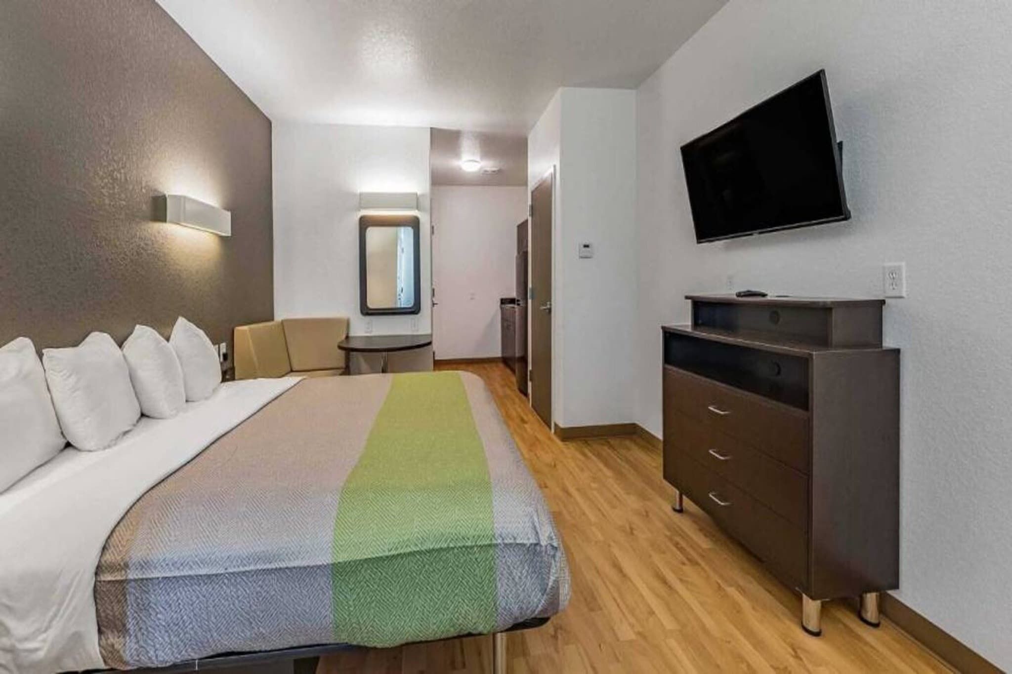 A hotel room with a bed, a dresser, a television, and a mirror.