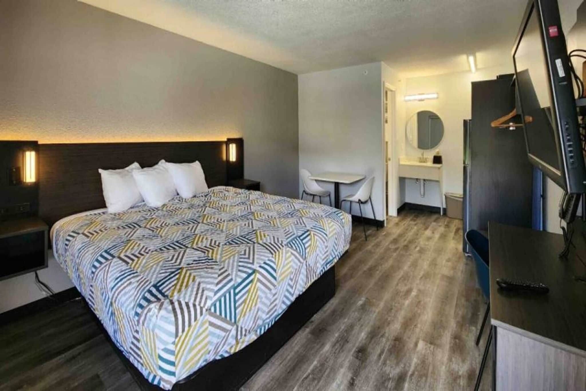 A hotel room with a bed, a desk, a chair, a TV, and a mirror.