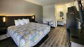 A hotel room with a bed, a desk, a chair, a TV, and a mirror.