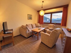Ein Hotelzimmer mit einer Sofagarnitur, einem Esstisch, einem Computer auf einem Schreibtisch und Blick auf Berge durch das Fenster.