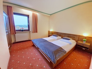 Ein Hotelzimmer mit Bett, Nachttischen, einem Fenster mit Vorhängen und einem Heizkörper.