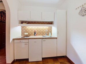 Een kleine keuken met witte kasten, een betegelde spatwand en een spoelbak.