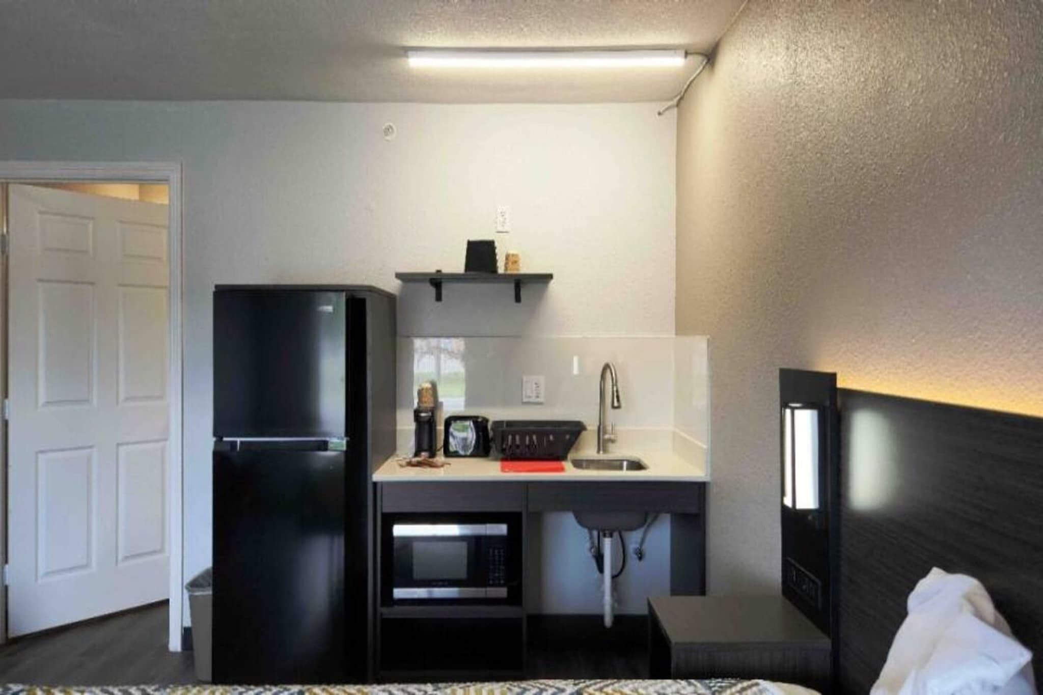 A compact hotel room with a kitchenette, including a refrigerator, microwave, and sink.