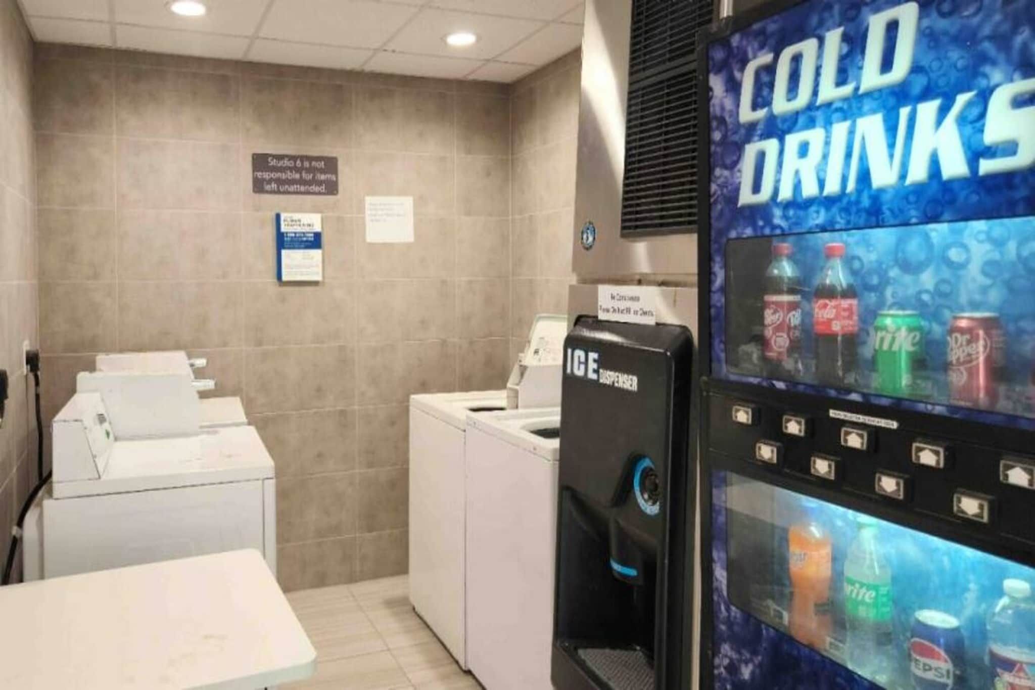 A laundry area with washing machines, a vending machine for cold drinks, and a sign indicating Studio 6 is not responsible for unattended items.