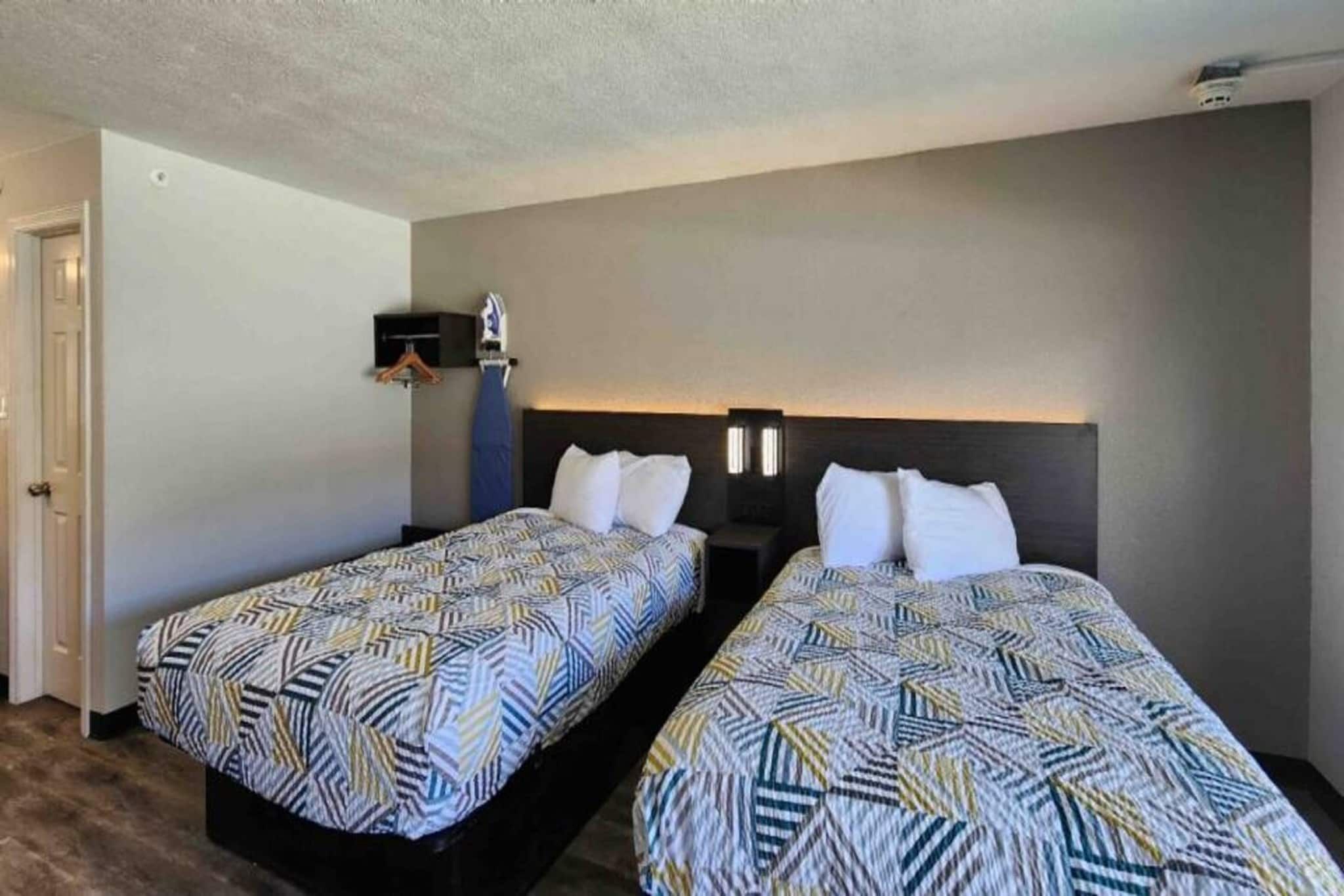 A hotel room with two beds, a wardrobe, and a nightstand with a lamp.
