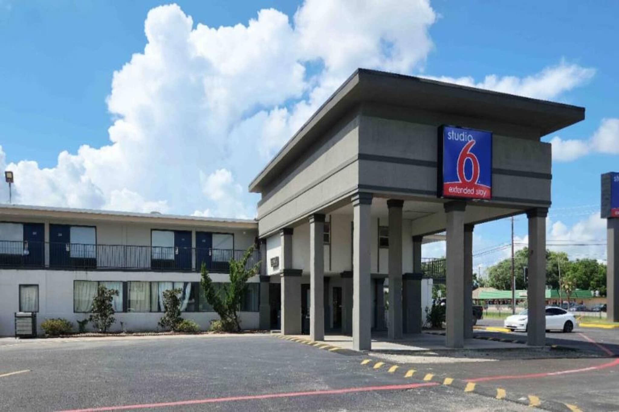 A hotel with a covered entrance, a sign indicating it's a Studio 6 extended stay, and a parking lot with a white car.