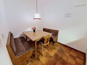 A dining area with a wooden table and chairs, a hanging light fixture, and a tiled floor. - Apartment Arnika by Interhome (Sankt Ulrich am Pillersee)
