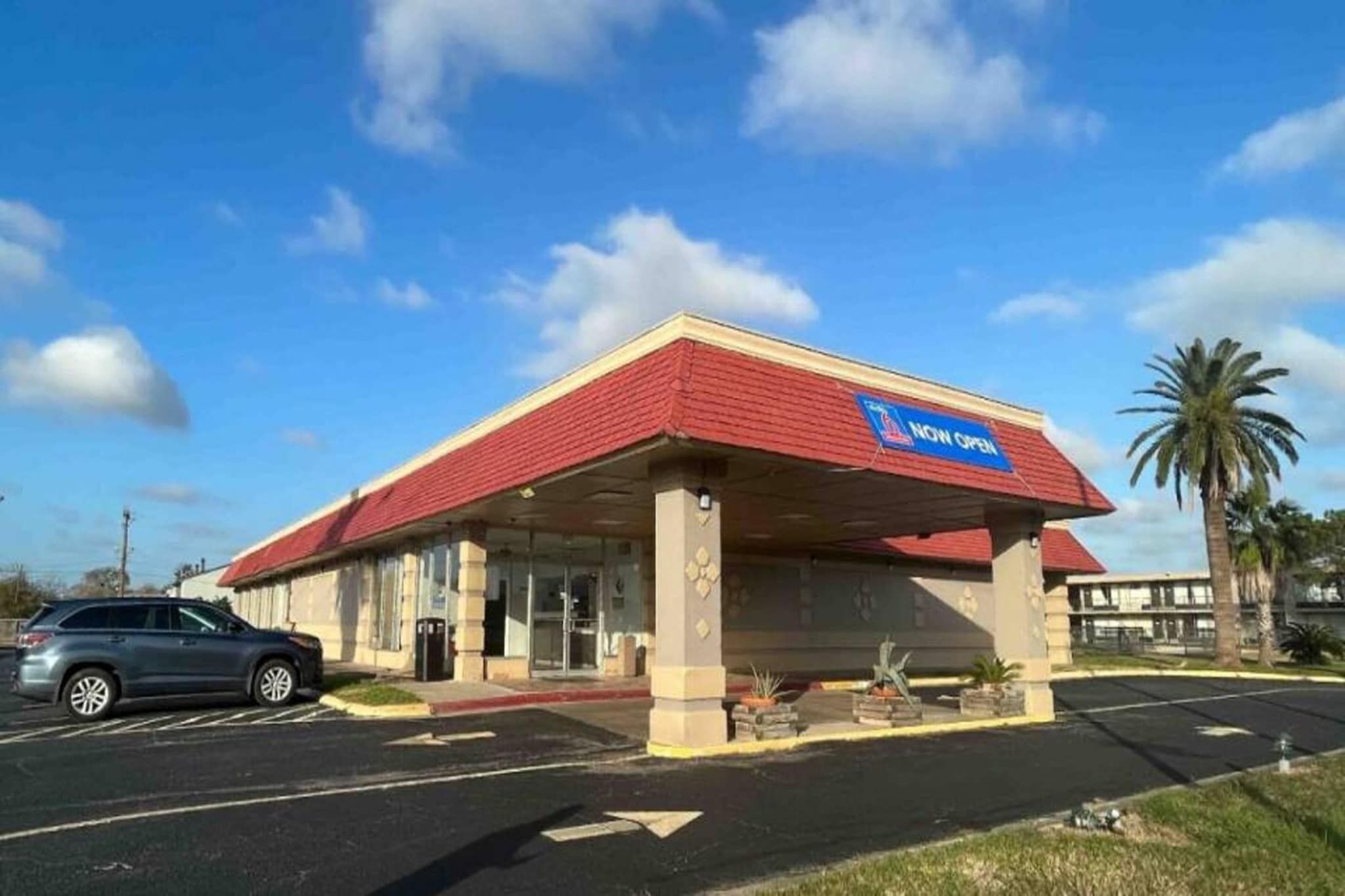 A building with a red roof and a blue sign indicating it's now open.