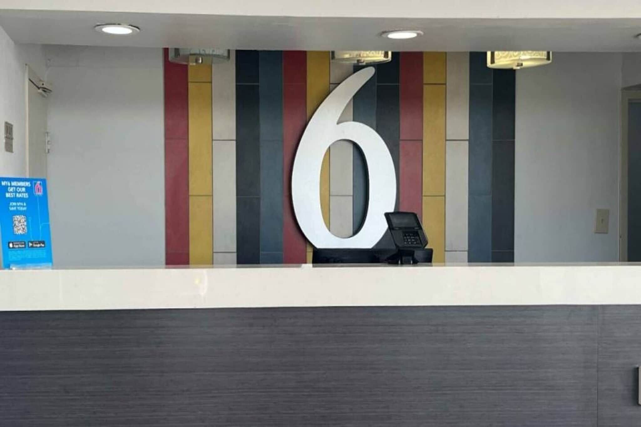 A reception desk with a large number '6' on the wall, a phone, and a blue informational sign.
