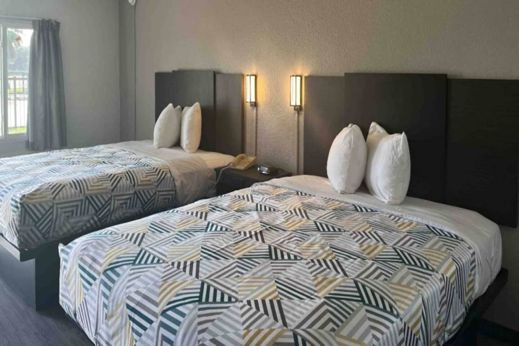 A hotel room with two beds, each with patterned bedding, a nightstand with a phone, and wall-mounted lights.