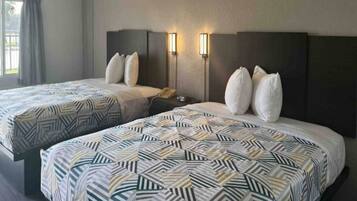 A hotel room with two beds, each with patterned bedding, a nightstand with a phone, and wall-mounted lights.