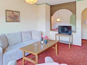 A living room with a sofa, a coffee table with a bottle and flowers, a TV on a stand, and a painting on the wall. - Kreuzblume by Interhome (Sankt Ulrich am Pillersee)