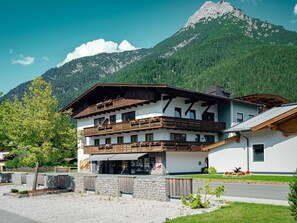 A two-story building with a balcony, a stone wall, and a mountain in the background. - Kreuzblume / App. 201 by Interhome (Sankt Ulrich am Pillersee)