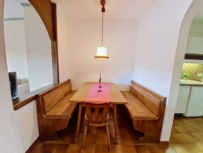 A dining area with a wooden table and bench seating, a hanging light fixture, and a kitchen area in the background. - Kreuzblume by Interhome (Sankt Ulrich am Pillersee)