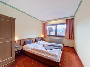 Ein Hotelzimmer mit Bett, Nachttisch, Kleiderschrank, einem Fenster mit Vorhängen und einer Heizung.