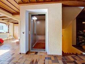 Ein Innenbereich mit Flurempfangsbereich, gefliestem Boden, einer Tür zu einem Zimmer und einer sichtbaren Decke mit Holzbalken.