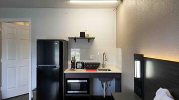 A compact kitchenette with a refrigerator, microwave, sink, and a small countertop.