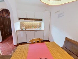 A compact kitchen with white cabinets, a countertop, and a sink. There is a small table with a pink placemat and a chair. - Edelweiß /App. 103 by Interhome (Sankt Ulrich am Pillersee)