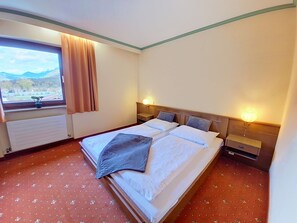 A hotel room with a bed, a window with curtains, a radiator, and a nightstand with a lamp. - Edelweiß /App. 103 by Interhome (Sankt Ulrich am Pillersee)