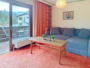 A room with a sofa, a table with potted plants, a window with curtains, and a painting on the wall. - Edelweiß by Interhome (Sankt Ulrich am Pillersee)
