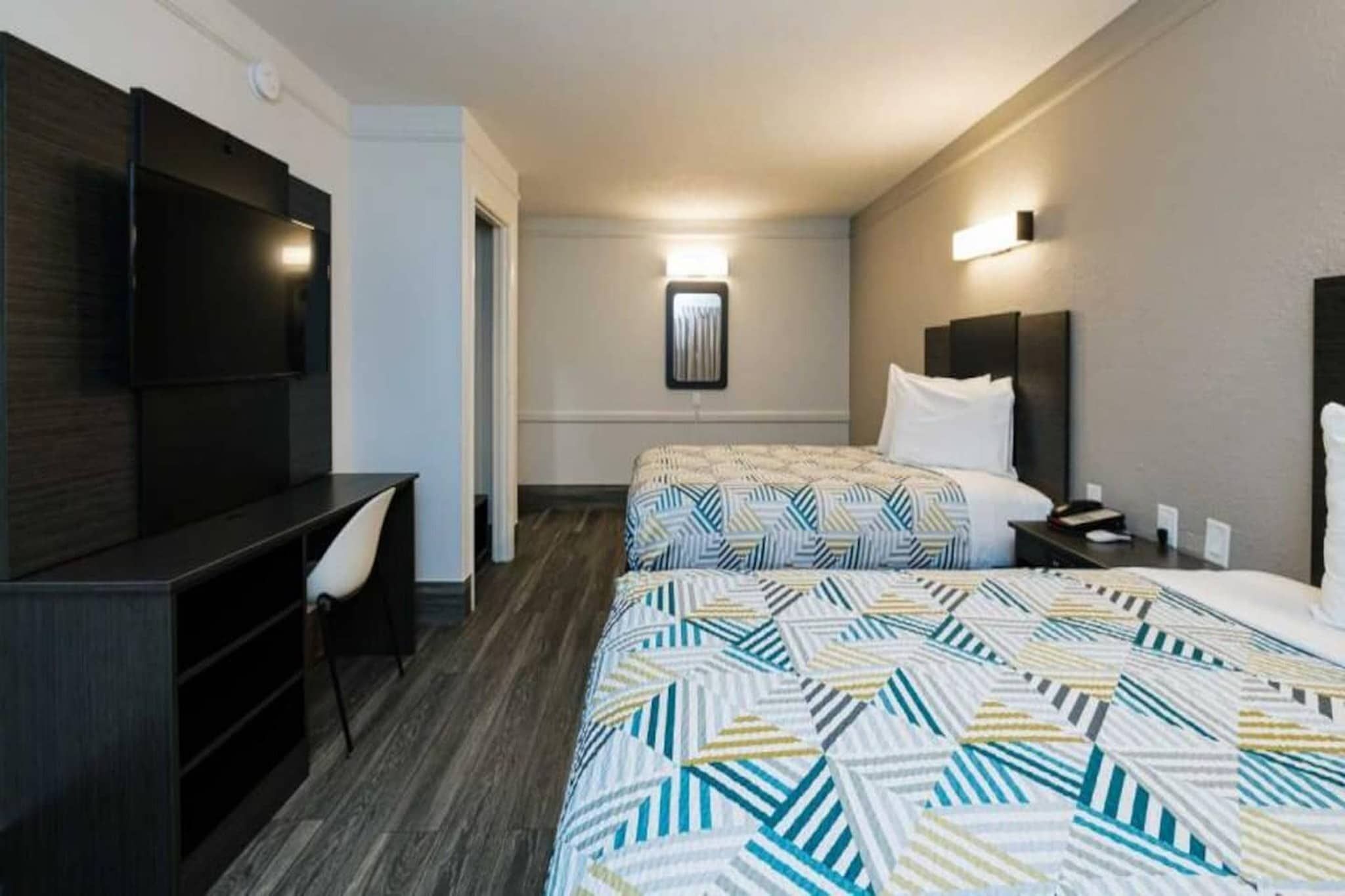 A hotel room with two beds, a desk, and a chair.