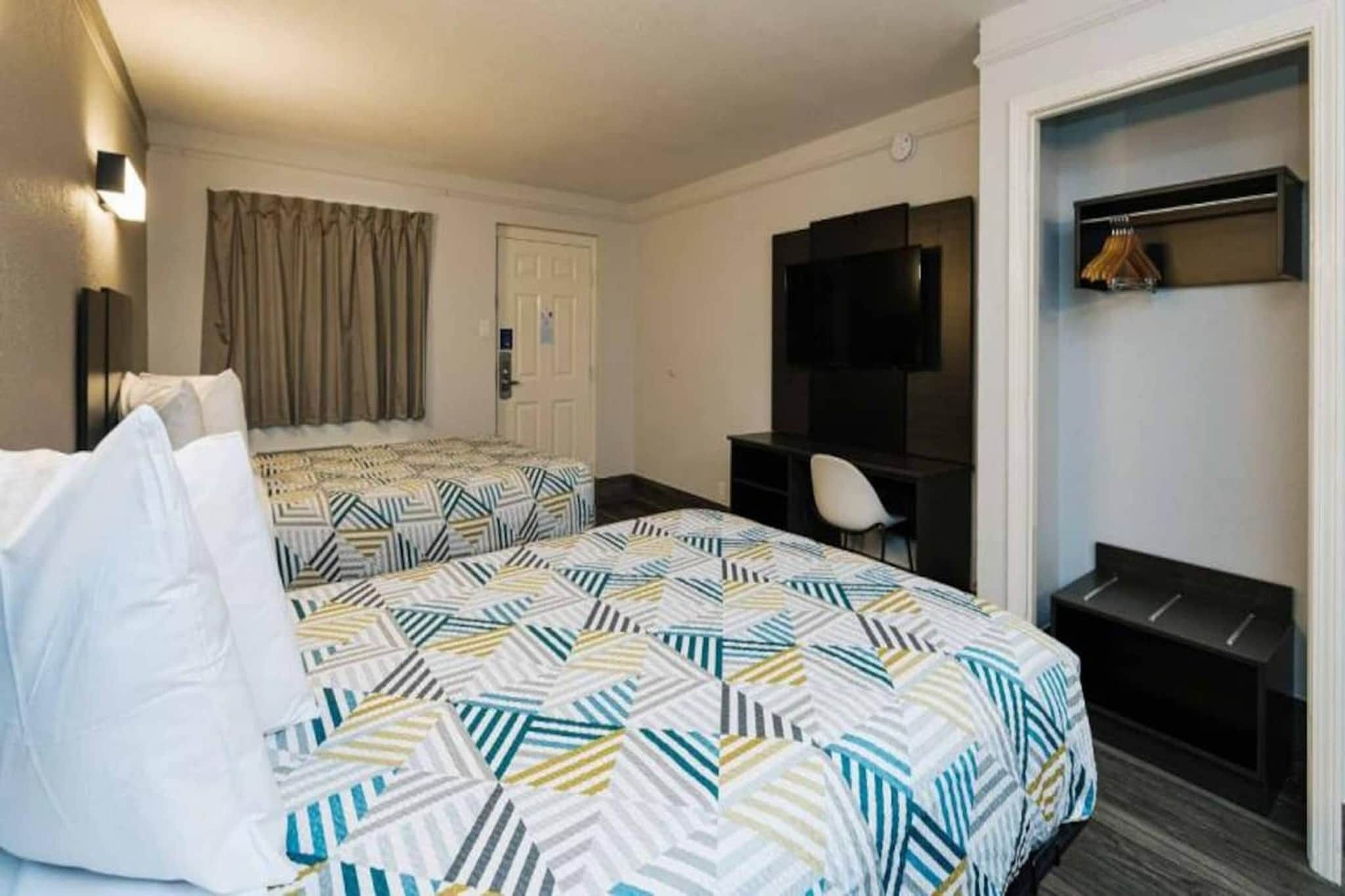 A hotel room with two beds, a desk, a TV, and a coat rack.